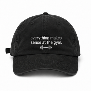 A black cotton baseball cap with white embroidered text reading 'everything makes sense at the gym.' and a small barbell graphic below, shown on a plain white background.